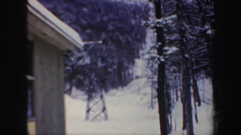 1962 New Hampshire frame with a snowy slope, tree line, tan building edge, and distant lift structure.