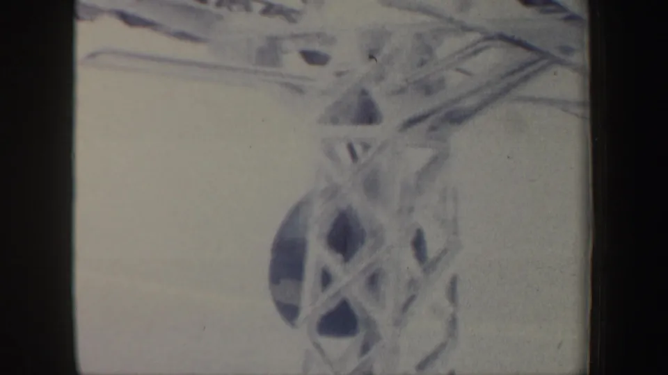 Soft 8mm frame showing a close, blurred view of ski lift wheel hardware and crossing cables in the snowy scene.