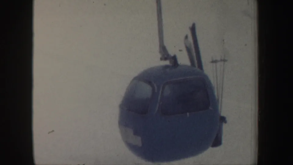 1962 New Hampshire frame showing a blue gondola cabin on a ski lift cable against a pale snowy background.