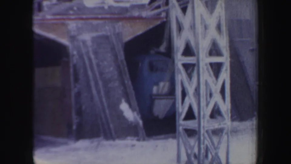 Snowy ski lift station area with stored skis and a metal tower, seen in vintage 8mm home-movie footage from New Hampshire.