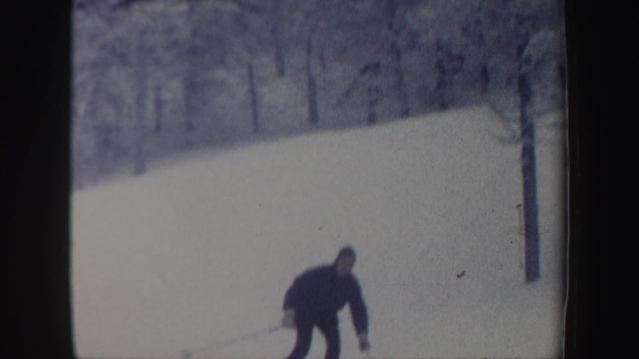 Distant skier descends a snowy New Hampshire slope in 1962 home-movie footage, with bare and pine trees in the background.