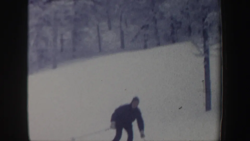 Distant skier descends a snowy New Hampshire slope in 1962 home-movie footage, with bare and pine trees in the background.