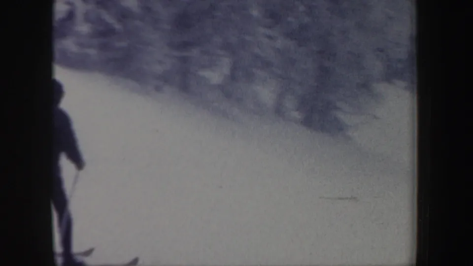 The skier appears partly cut off at the left edge while moving along a snowy wooded slope in the New Hampshire home movie.