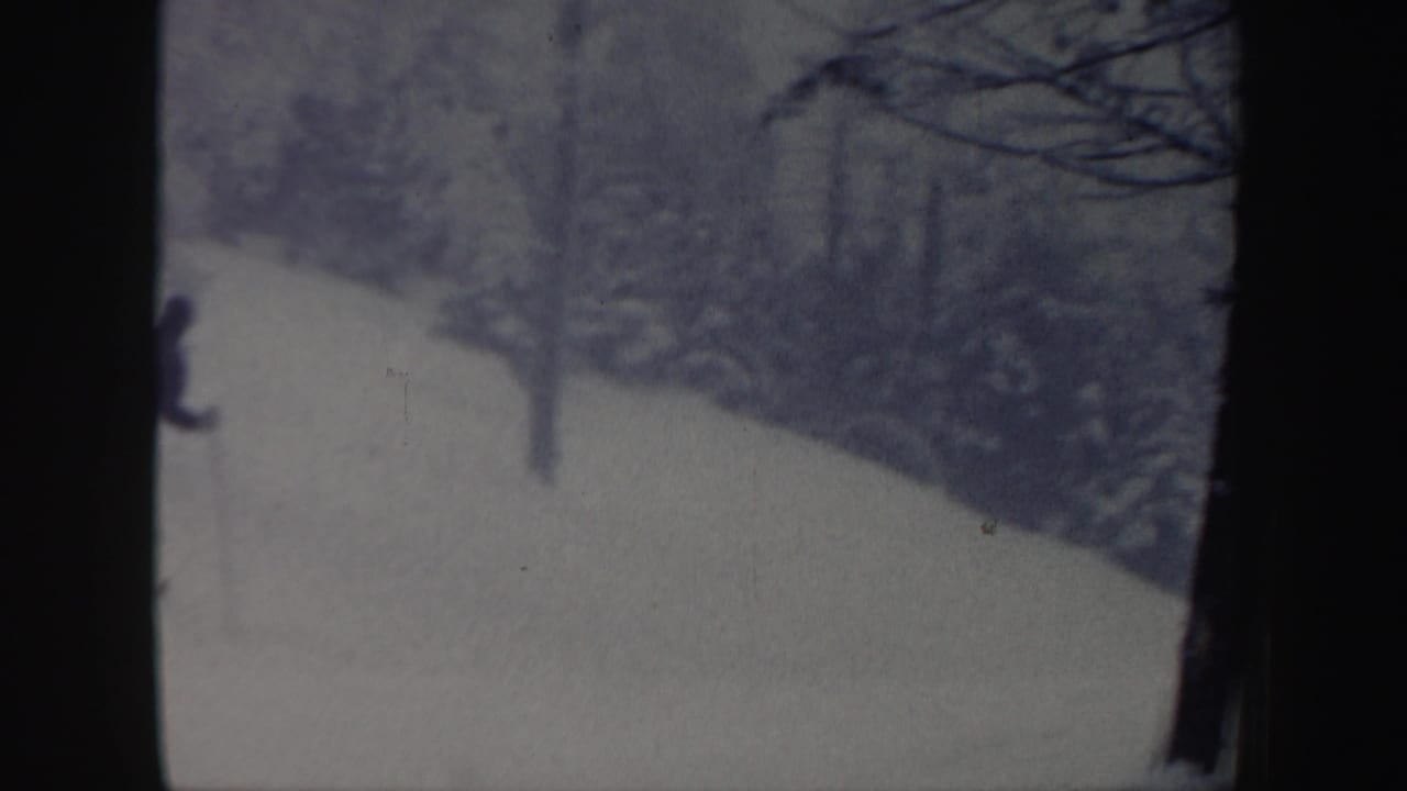 1962 New Hampshire 8mm frame showing a snowy hill bordered by trees, with a distant skier partly visible near the left edge.