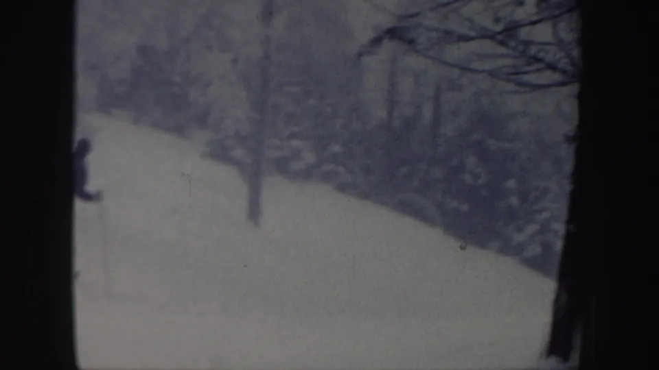 1962 New Hampshire 8mm frame showing a snowy hill bordered by trees, with a distant skier partly visible near the left edge.