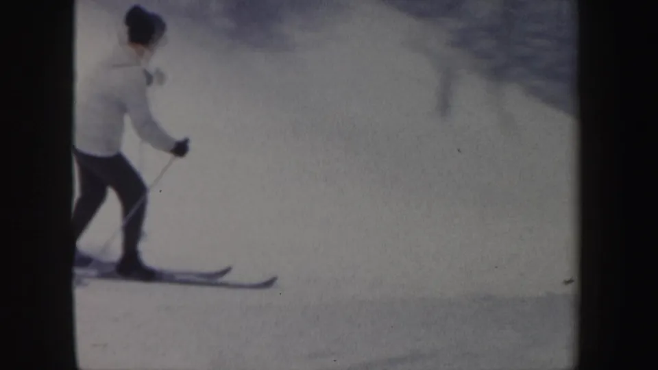 A distant skier in a white jacket glides across a bright snowy New Hampshire slope in this 1962 8mm frame.