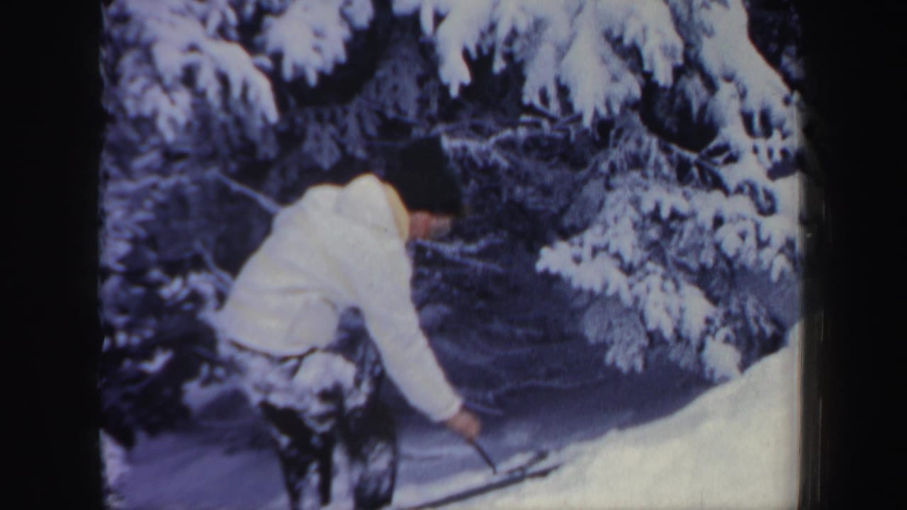 Woman in a white jacket climbs a snowy hill beside snow-covered evergreens.