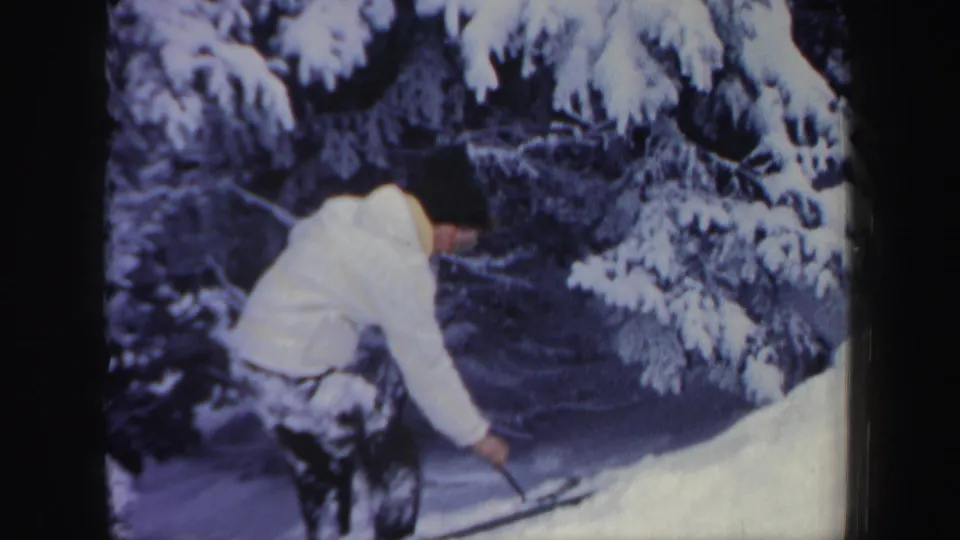 In 1962 New Hampshire home-movie footage, a woman in winter clothing uses a ski pole while climbing a snowy bank.