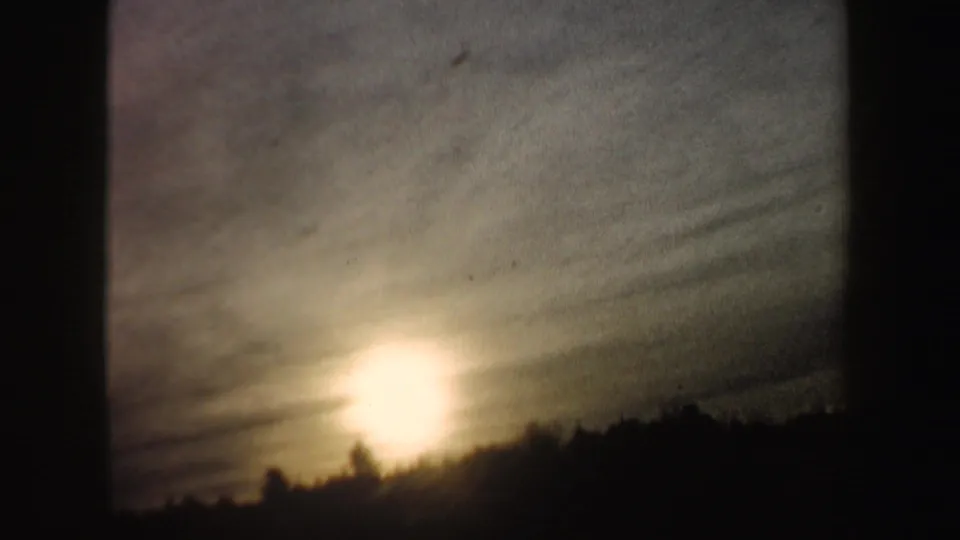 The clip ends on a low sun glowing through clouded sky over a dark winter tree line in the same home-movie sequence.