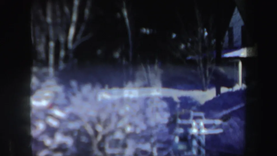 1962 New Hampshire 8mm view of snow-covered property with bare trees, dark house edge, and a small lift-like structure in the foreground.