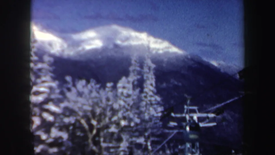 1962 New Hampshire winter frame showing a snowy mountain ridge, frosted trees, and ski lift equipment under a deep blue sky.