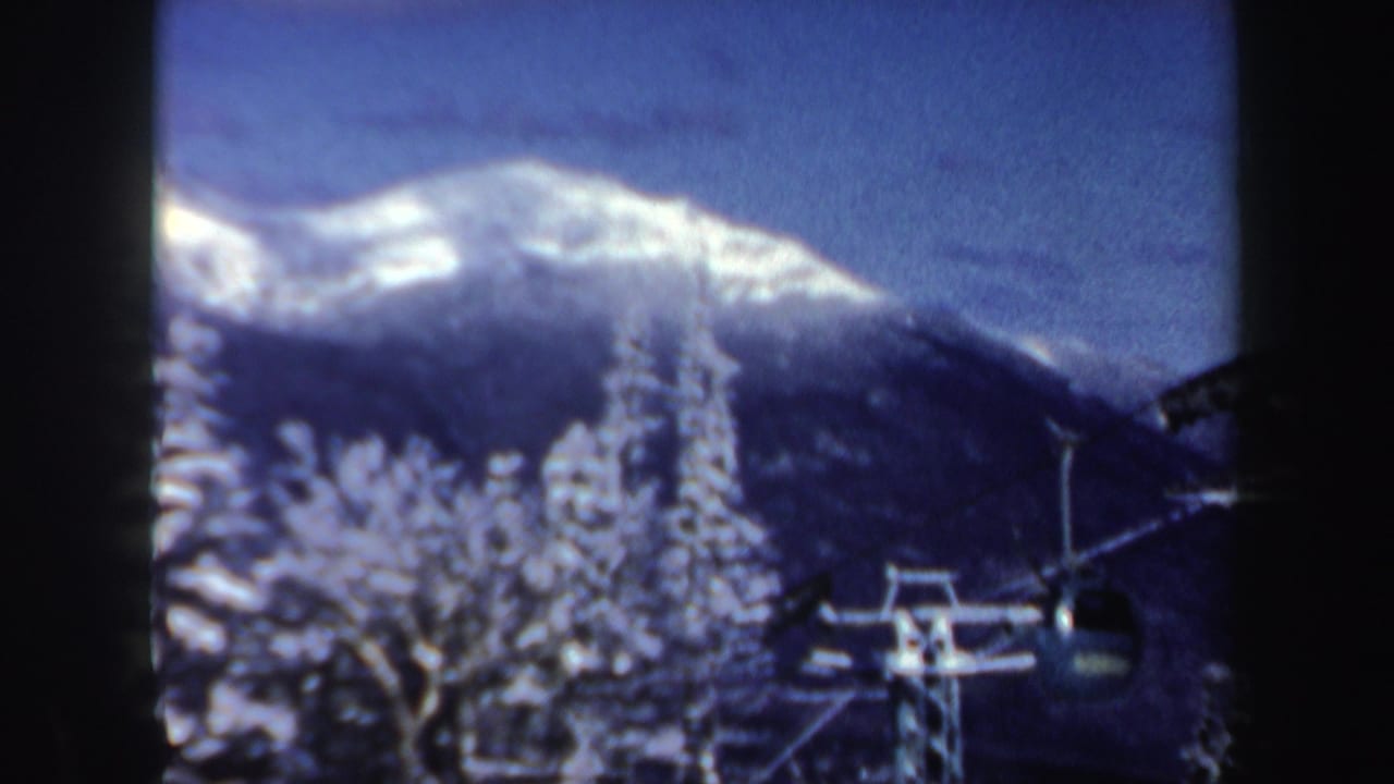 Ski lift gondola and snowy trees in front of a sunlit mountain ridge.