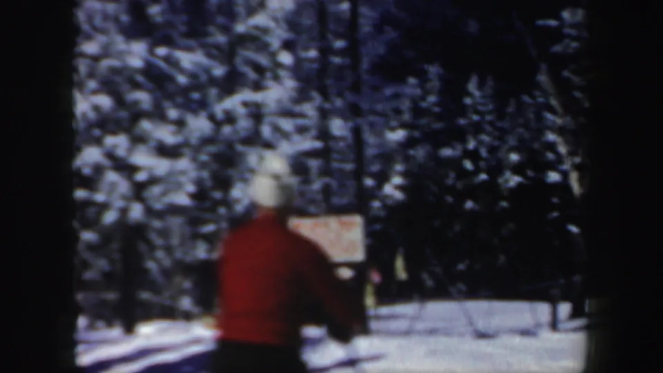 1962 New Hampshire home-movie frame showing a skier in a red sweater and light hat passing near the camera.