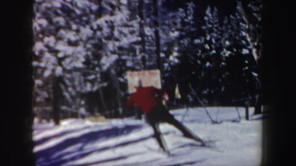 1962 New Hampshire 8mm frame of a skier in a red sweater turning across a snowy slope below a ski lift.
