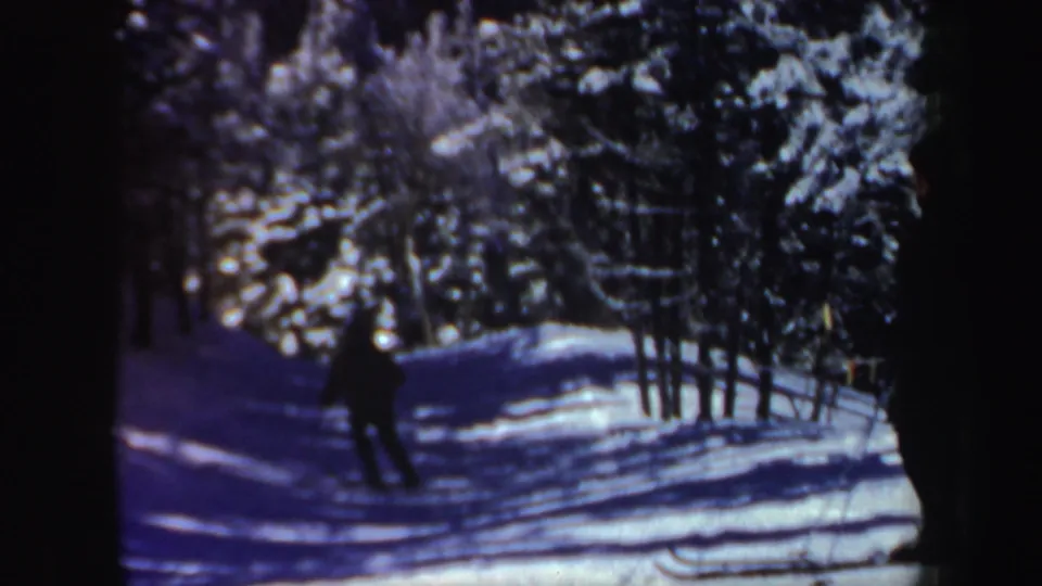 The skier recedes down a blue-shadowed snowy trail lined with dense winter evergreens in New Hampshire.