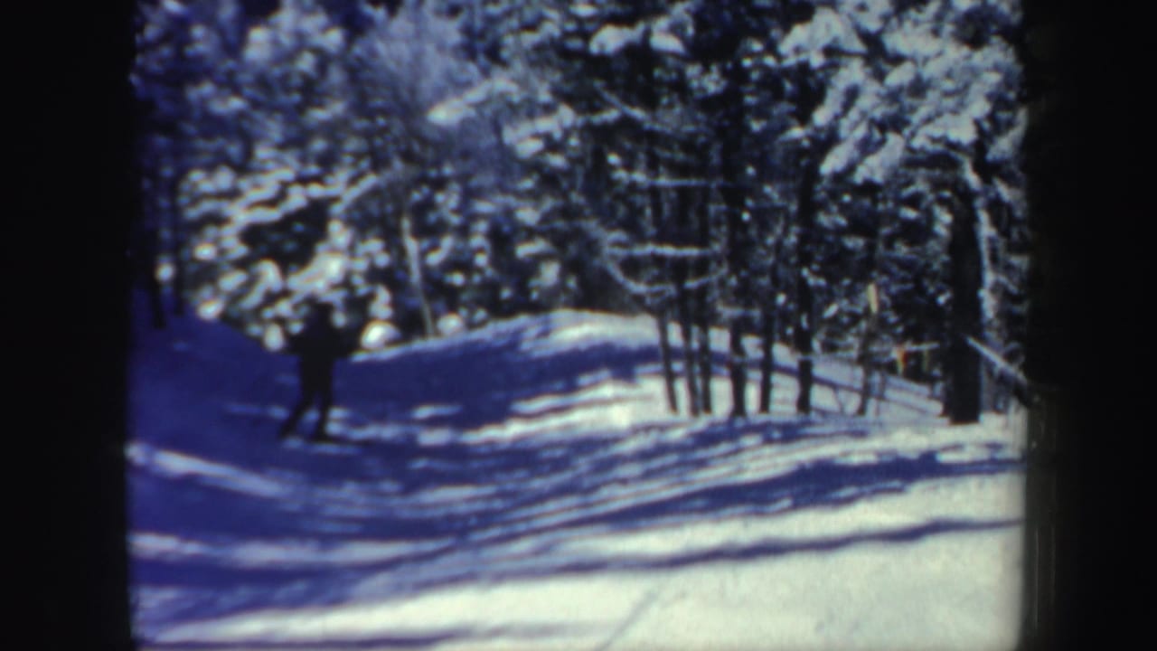 A skier appears farther down a snow-covered wooded slope in metadata-supported 1962 New Hampshire footage.