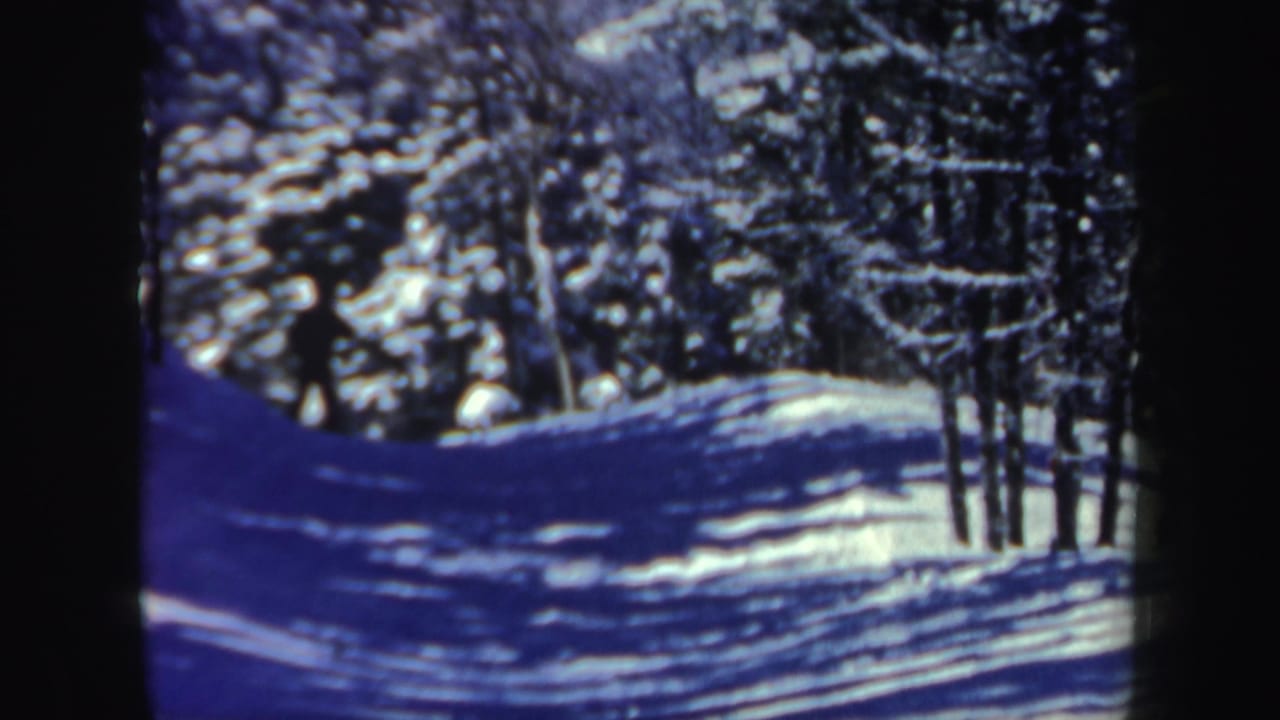 A blue-tinted 8mm frame shows the snowy forest trail and surrounding trees from the 1962 New Hampshire ski scene.