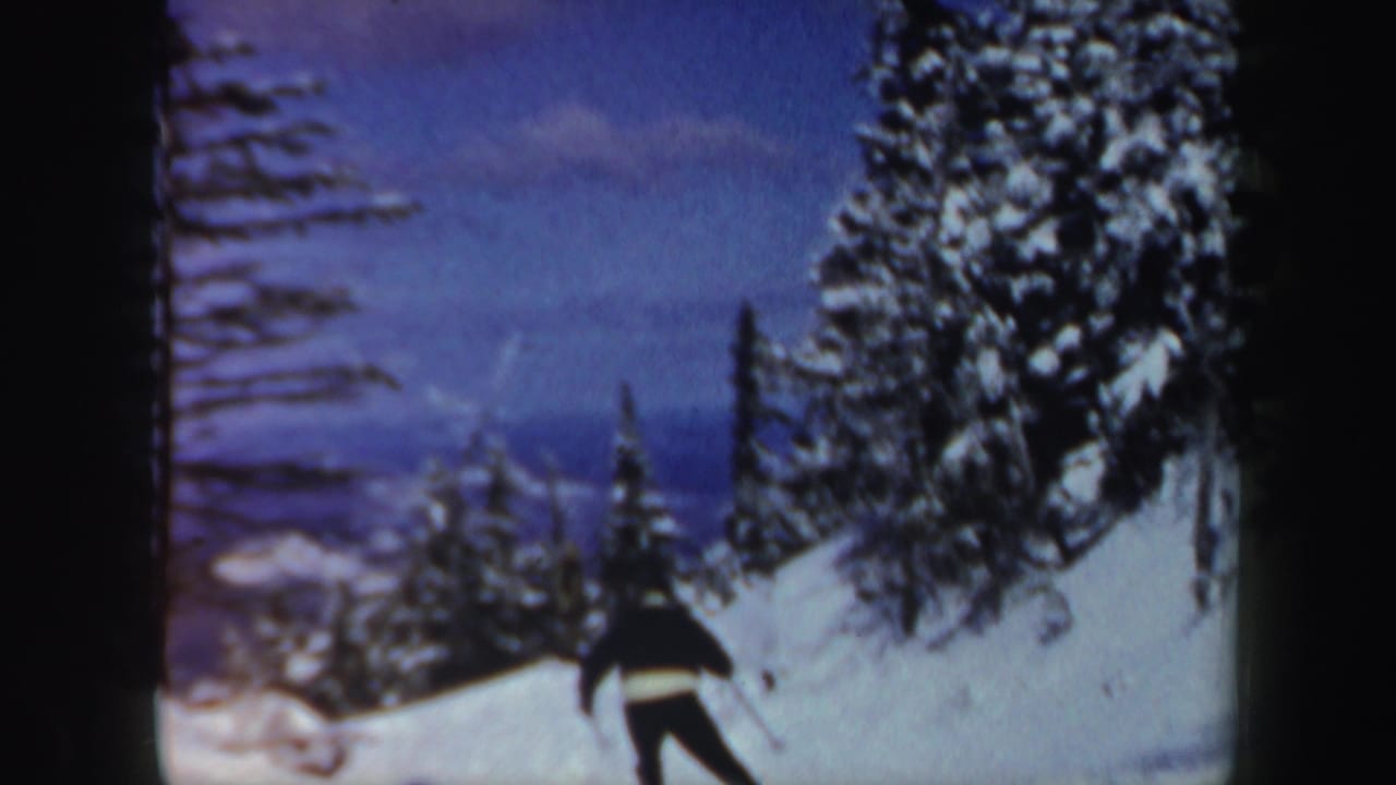 The skier continues downhill beneath heavy pines, with distant snowy New Hampshire ridges visible through soft 8mm color.