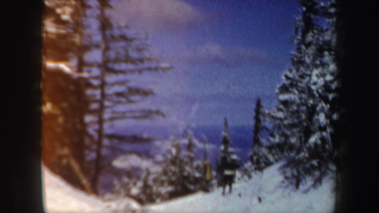 A distant skier appears near snow-covered evergreens in a 1962 New Hampshire winter mountain scene.