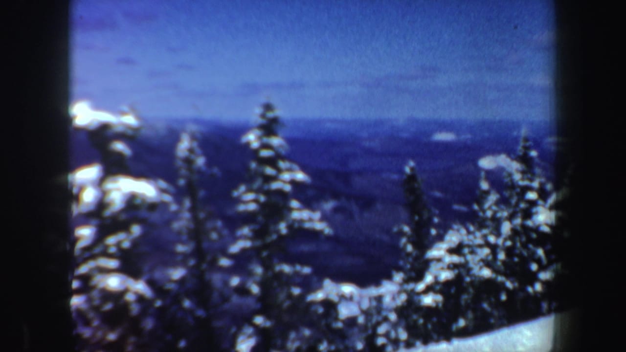 1962 New Hampshire 8mm frame with snowy conifer tops, distant ridges, and a blue sky seen from a winter overlook.