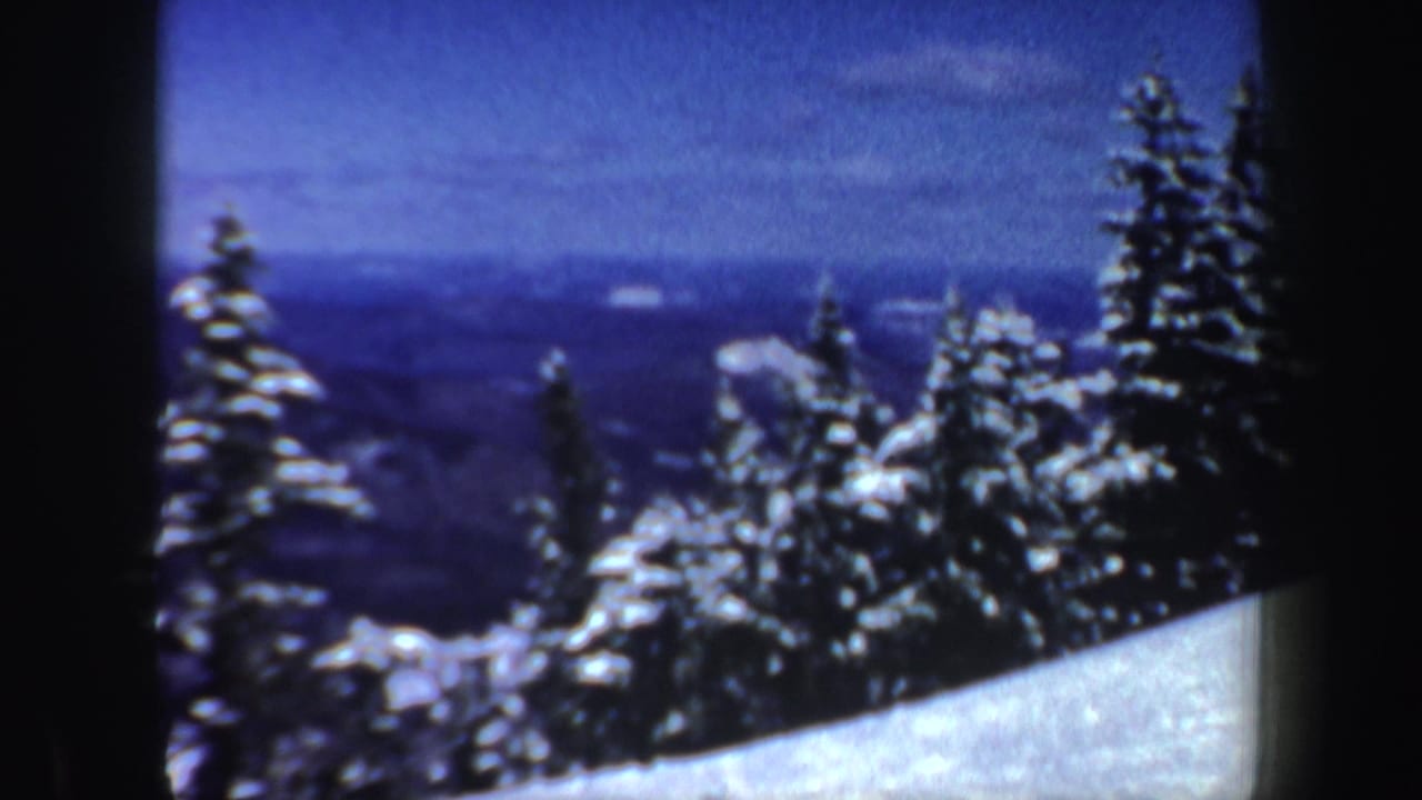 1962 New Hampshire 8mm frame showing a snowy evergreen slope with distant hills and a blue winter sky beyond.
