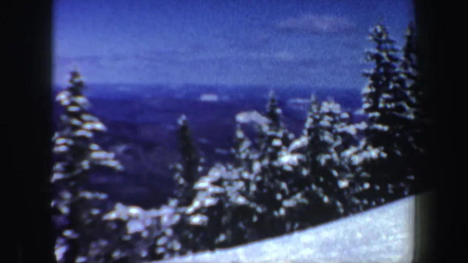 1962 New Hampshire 8mm frame showing a snowy evergreen slope with distant hills and a blue winter sky beyond.