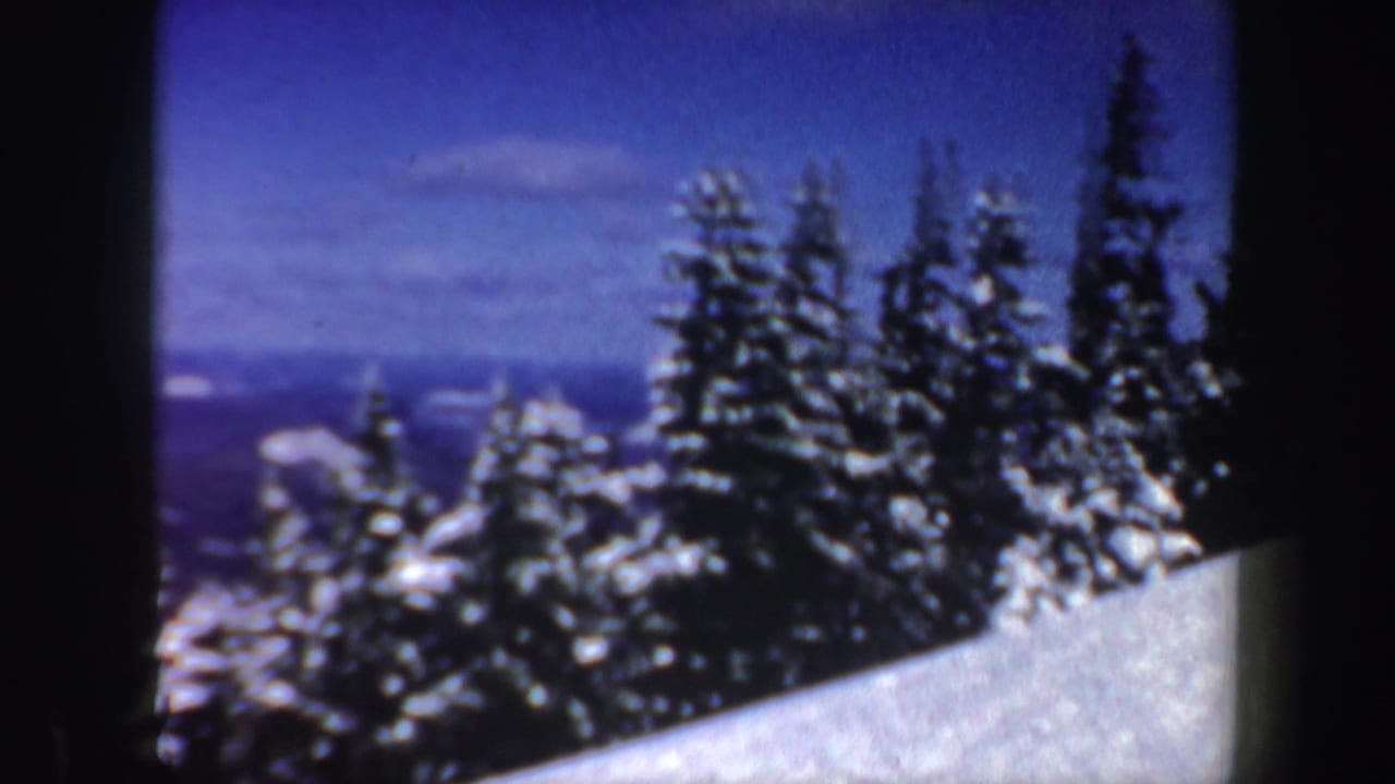 1962 New Hampshire 8mm frame with snow-covered evergreens, a sloped snowbank, and distant blue mountain ridges.