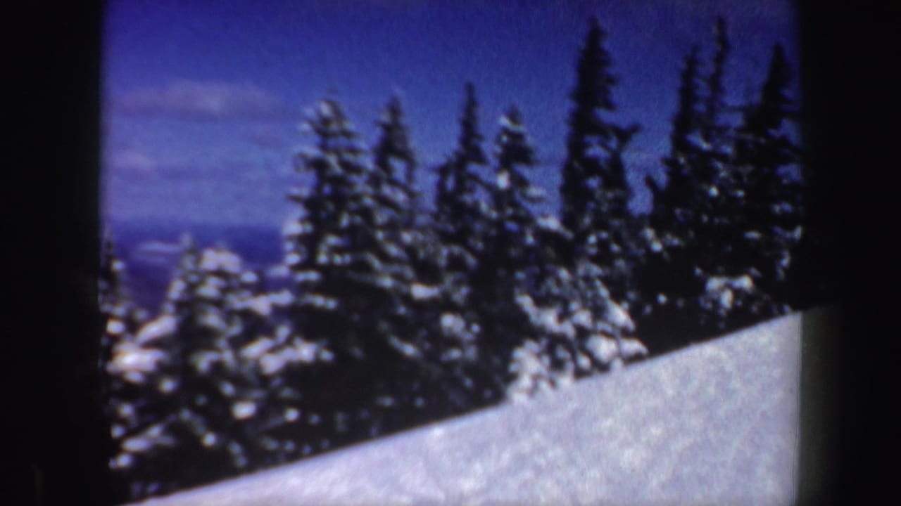 1962 New Hampshire 8mm frame showing a snowy mountain slope bordered by dark evergreen trees under a blue sky.