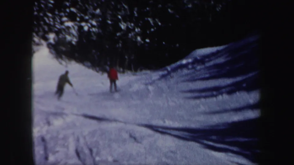 Two men practice on a snowy New Hampshire slope in 1962, with one wearing a red coat against the dark tree line.