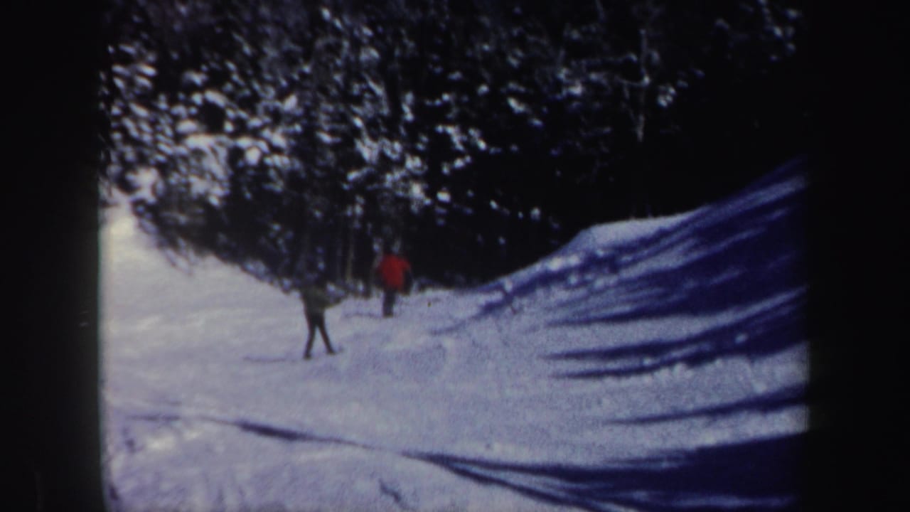 Distant figures practice on a wooded New Hampshire snow slope in this 1962 8mm home-movie frame.