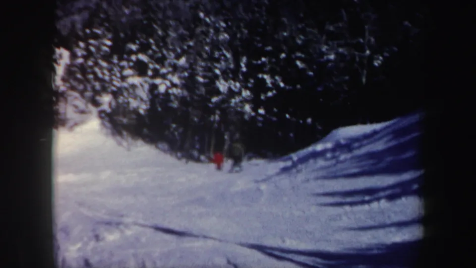 Two distant men near the evergreen edge of a snowy New Hampshire slope, filmed on 8mm in 1962.