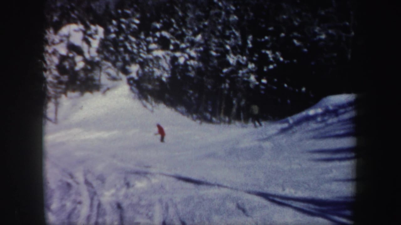 1962 New Hampshire 8mm frame showing a distant skier in red crossing a sunlit snowy slope near evergreen trees.