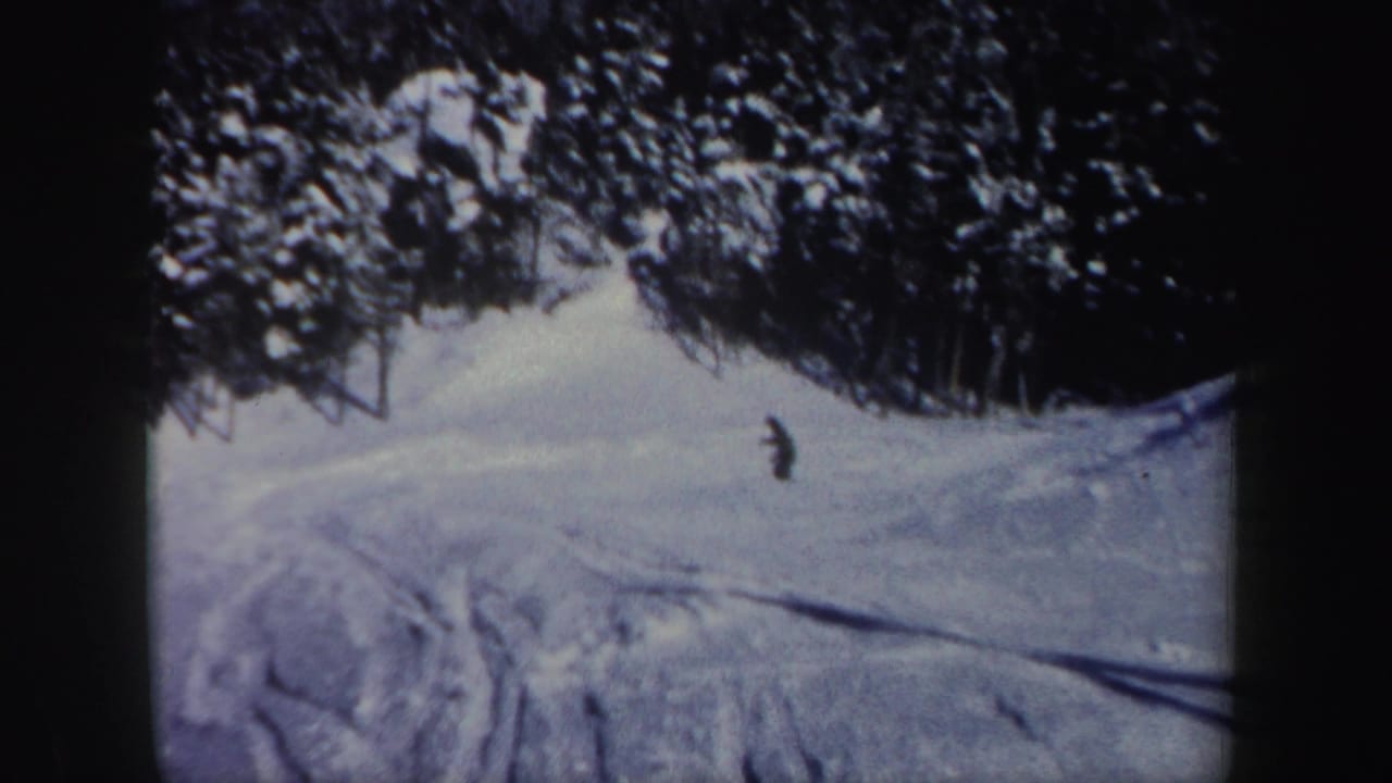 1962 New Hampshire home-movie frame with a distant skier descending a snowy run edged by evergreen trees.