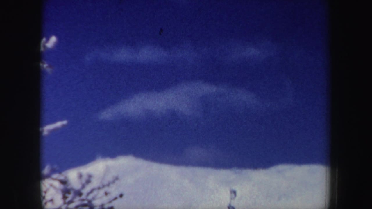 1962 New Hampshire home-movie frame showing a small skier near a bright snow ridge under clear blue sky.