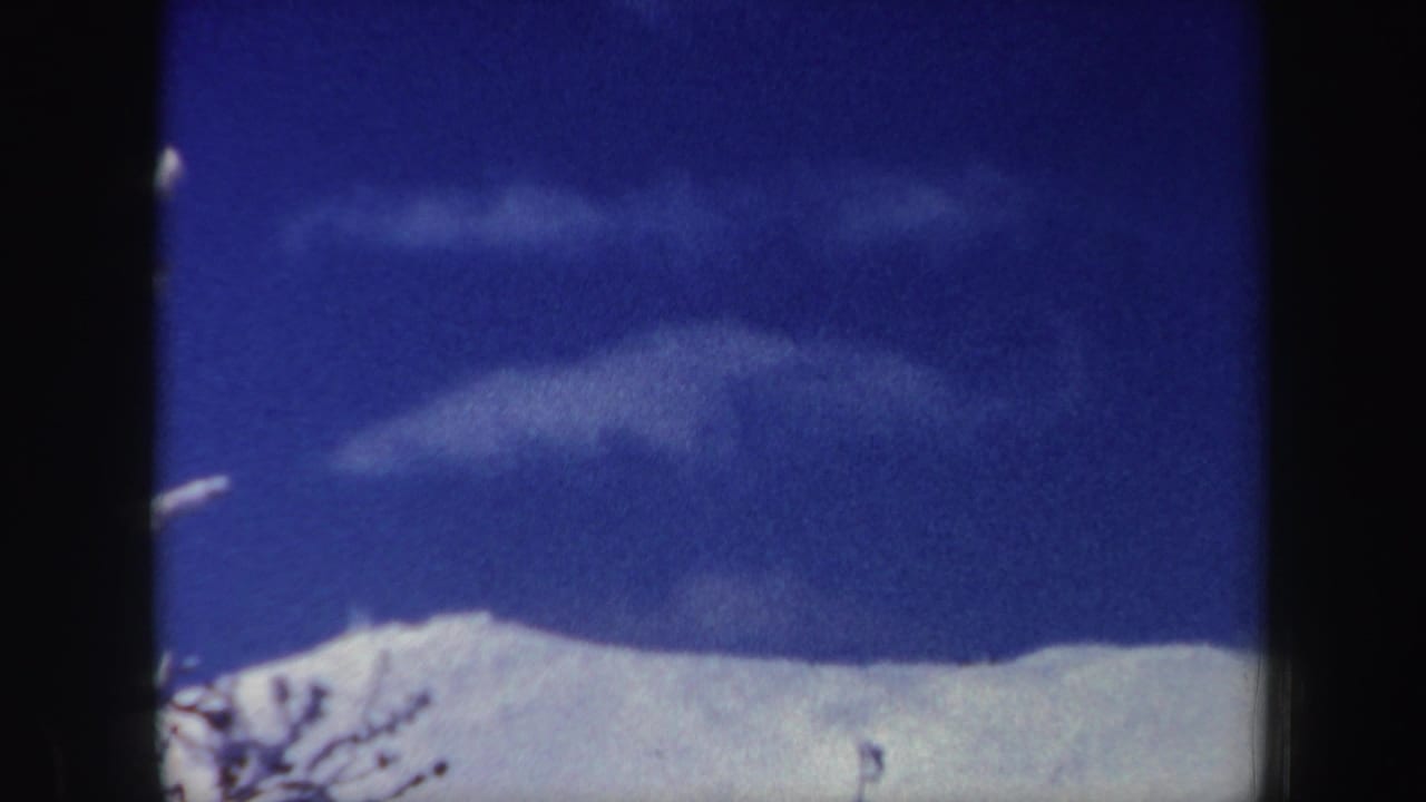 1962 New Hampshire 8mm frame showing a snowy mountain ridge under a saturated blue sky with light cloud bands.
