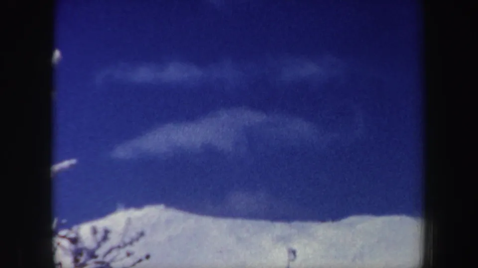 1962 New Hampshire 8mm frame showing a snowy mountain ridge under a saturated blue sky with light cloud bands.