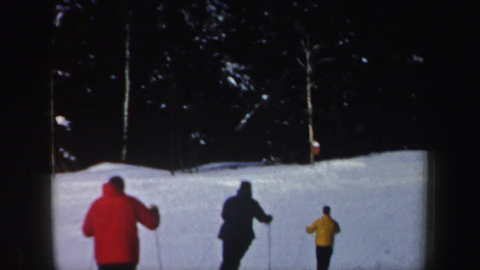 Three adult skiers in red, dark, and yellow outerwear move across a snowy New Hampshire slope in the 1962 home movie.