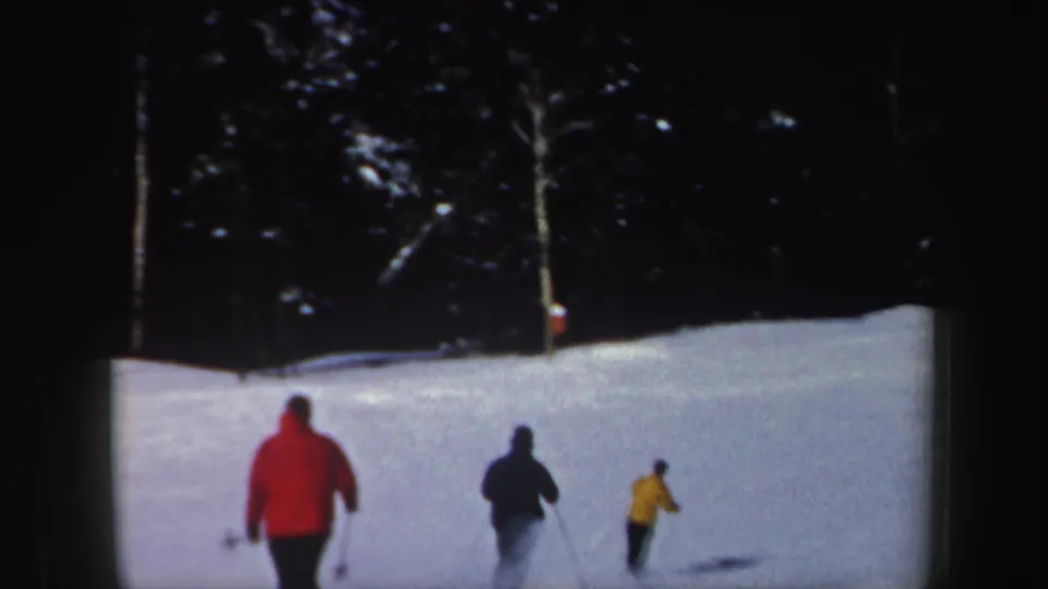 Three skiers in red, dark, and yellow outerwear descend a snowy New Hampshire slope in 1962 home-movie footage.