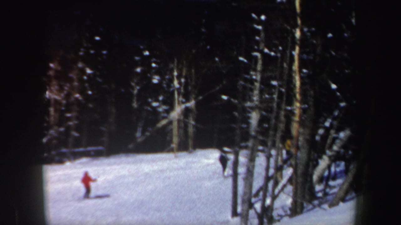 A red-jacketed skier moves across the lower snowy slope near bare trees in New Hampshire 1962 home-movie footage.