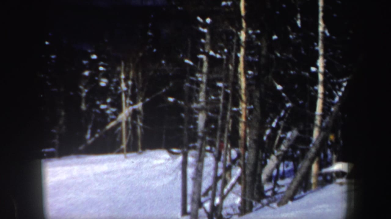 1962 New Hampshire 8mm frame of a snow-covered ski slope and dark trees, with the skier no longer clearly visible.