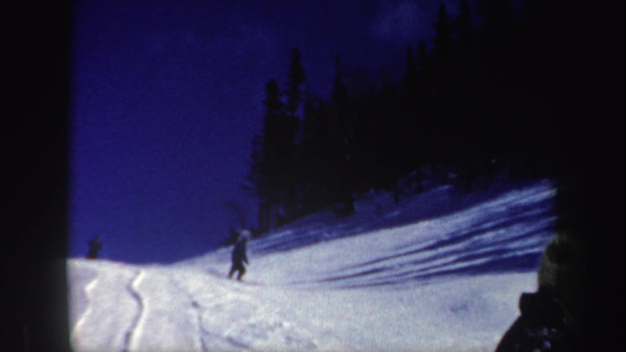 1962 New Hampshire 8mm frame with a distant skier on a snowy hillside, tree shadows, ski tracks, and a saturated blue sky.
