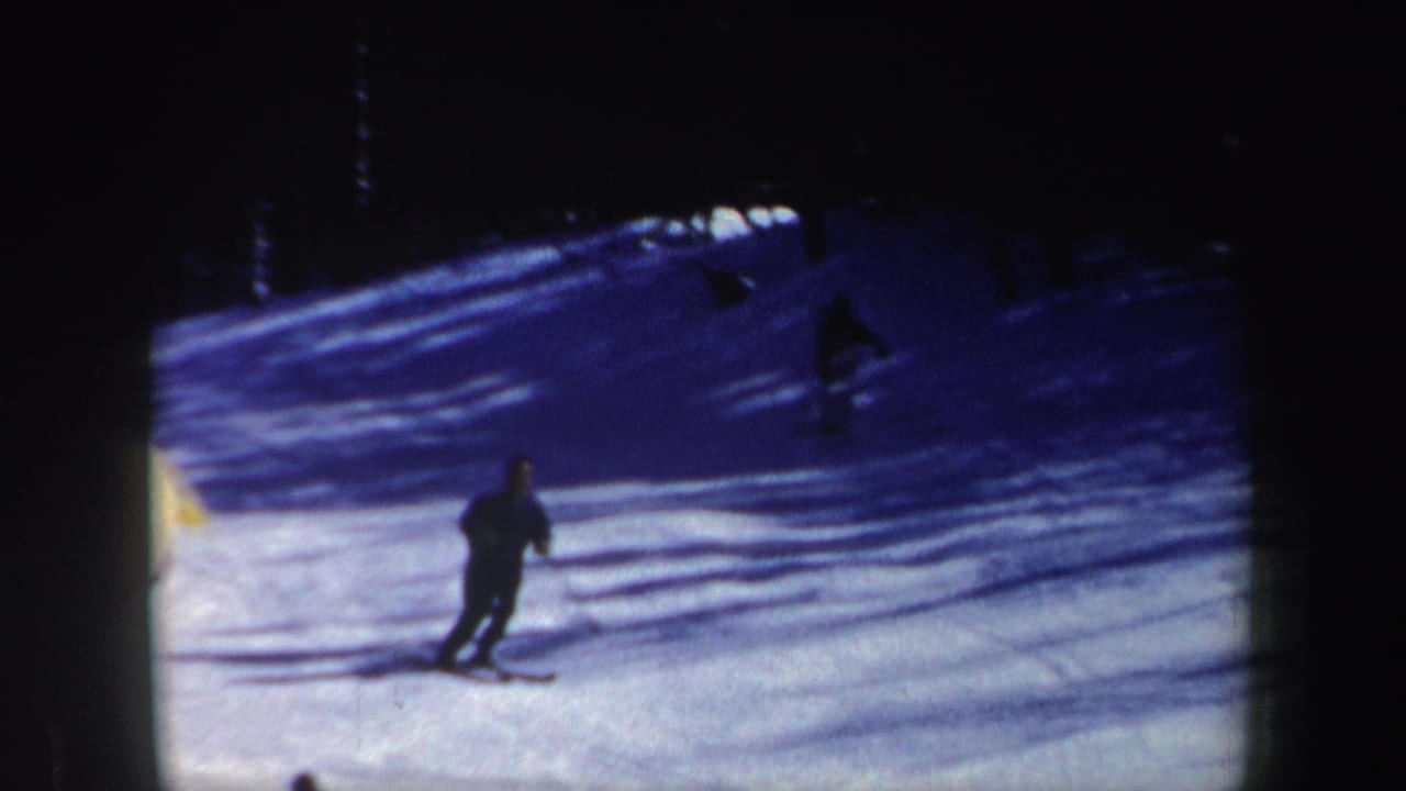 1962 New Hampshire 8mm frame showing a skier in dark clothing moving downhill across snow near a shadowed tree line.