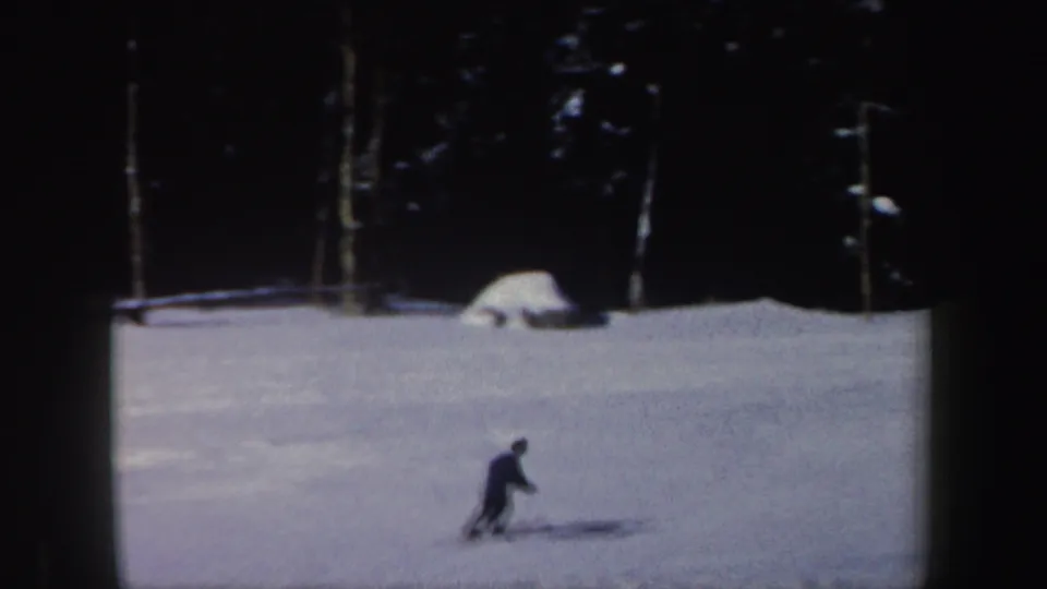 1962 New Hampshire 8mm frame showing the skier lower on the hill, with snow-covered ground and dark forest in the background.
