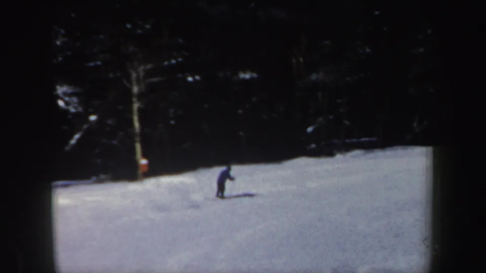 A lone adult skier appears small on a snowy New Hampshire slope in 1962 home-movie footage, with dark forest behind.