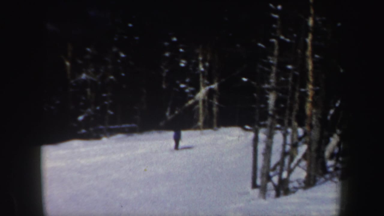 A lone skier moves across a snowy wooded slope, seen from a distance in 1962 New Hampshire 8mm footage.