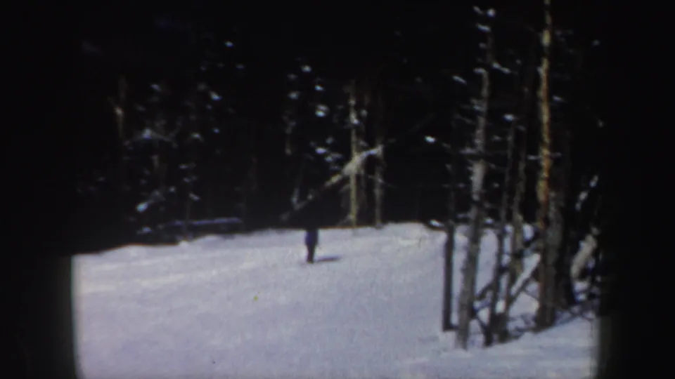 A lone skier moves across a snowy wooded slope, seen from a distance in 1962 New Hampshire 8mm footage.