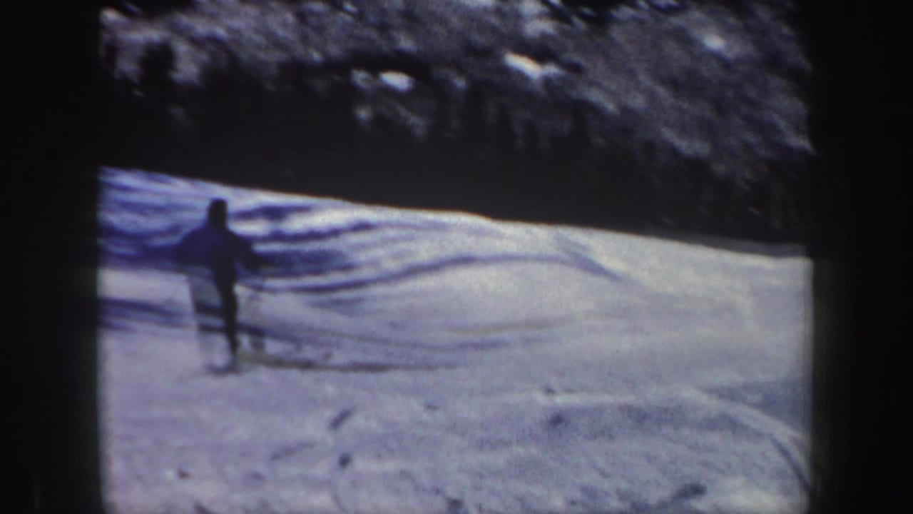 The adult skier moves away from the camera across tracked snow, with wooded hillside in vintage New Hampshire footage.
