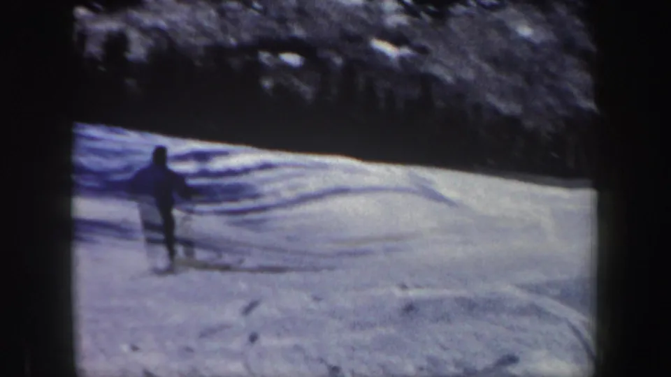 The adult skier moves away from the camera across tracked snow, with wooded hillside in vintage New Hampshire footage.