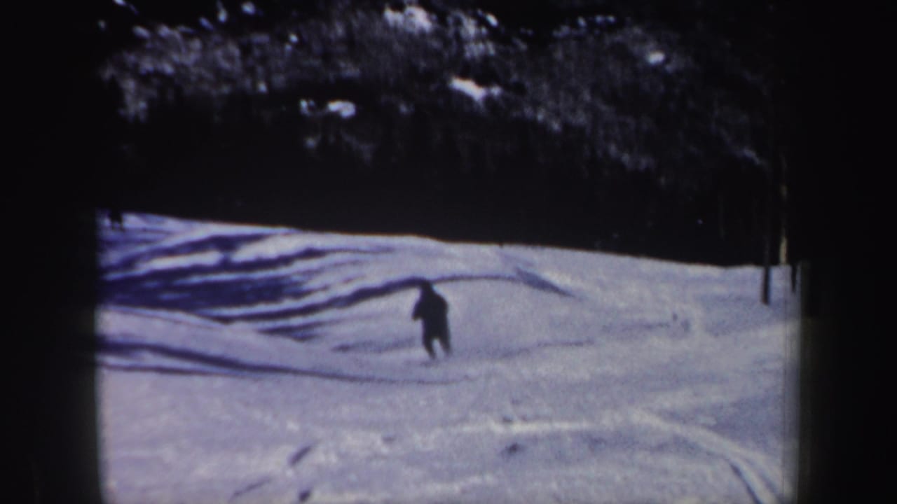 1962 New Hampshire 8mm frame showing the skier turning across tracked snow, with deep tree shade above the open slope.