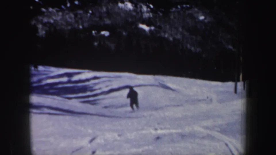 1962 New Hampshire 8mm frame showing the skier turning across tracked snow, with deep tree shade above the open slope.